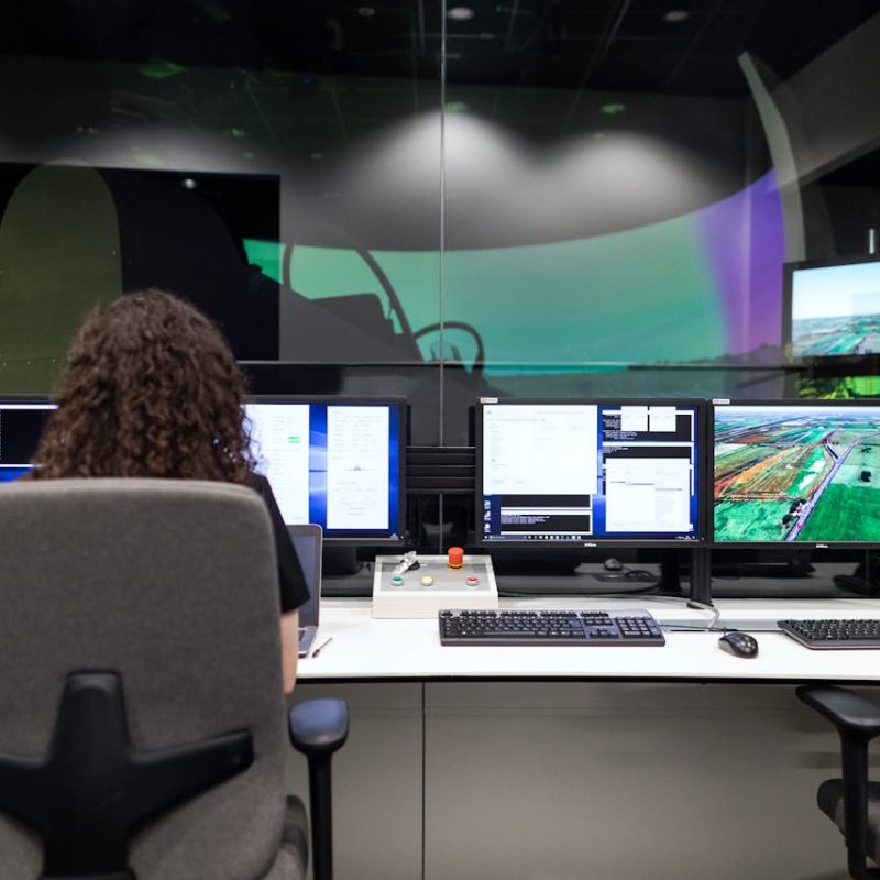 Person working at a control station with multiple monitors displaying data and images, illustrating technology innovation in IT and business environments.